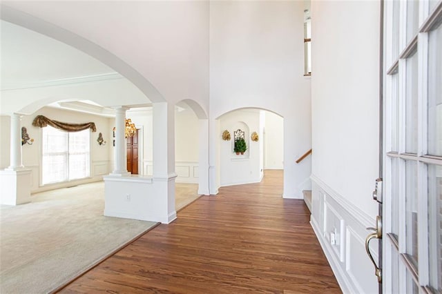 hall with dark hardwood / wood-style flooring, a towering ceiling, and decorative columns