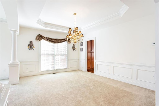 carpeted spare room with decorative columns, ornamental molding, an inviting chandelier, and a tray ceiling