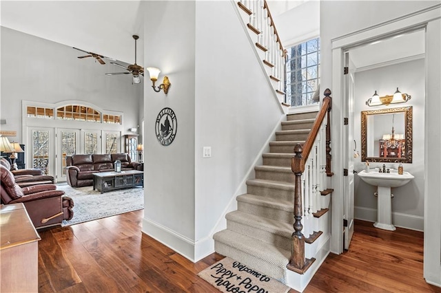 stairs with hardwood / wood-style floors, a towering ceiling, and ceiling fan