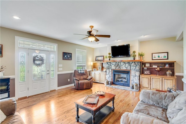 living room featuring ceiling fan, a stone fireplace, and light wood-type flooring