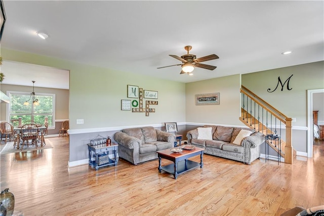 living room featuring ceiling fan with notable chandelier and light wood-type flooring