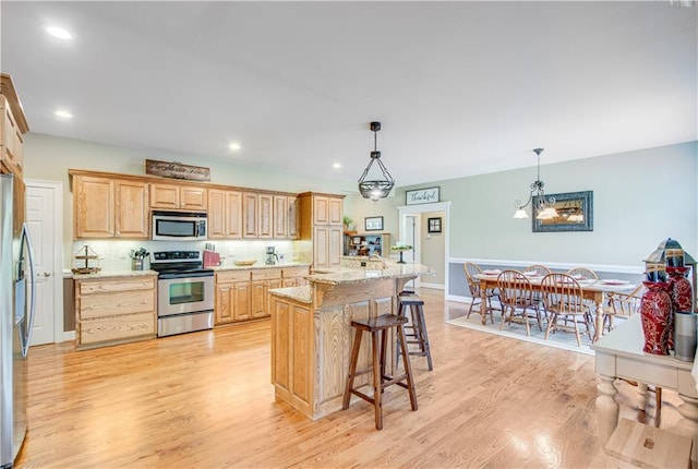 kitchen with appliances with stainless steel finishes, light wood-type flooring, light stone counters, a notable chandelier, and decorative light fixtures