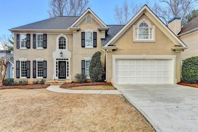 colonial house with a shingled roof, concrete driveway, a chimney, and stucco siding