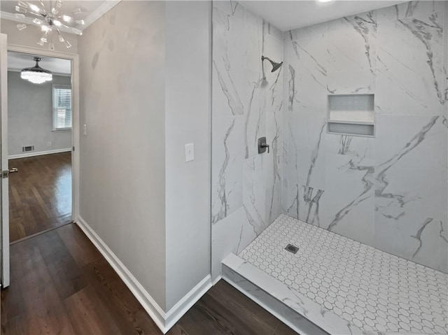 bathroom with a tile shower, a notable chandelier, wood-type flooring, and ornamental molding