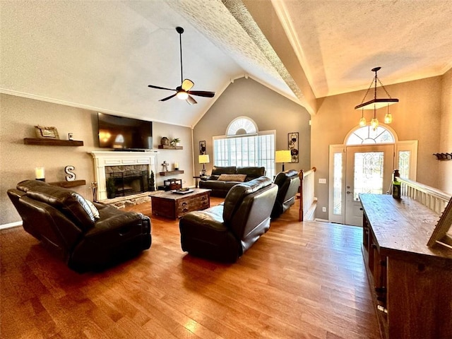 living room with hardwood / wood-style floors, a textured ceiling, high vaulted ceiling, ceiling fan, and a fireplace