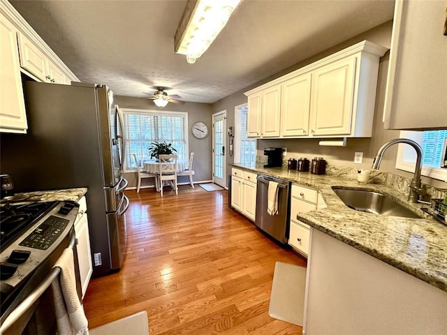 kitchen with stainless steel appliances, white cabinetry, sink, and light hardwood / wood-style flooring