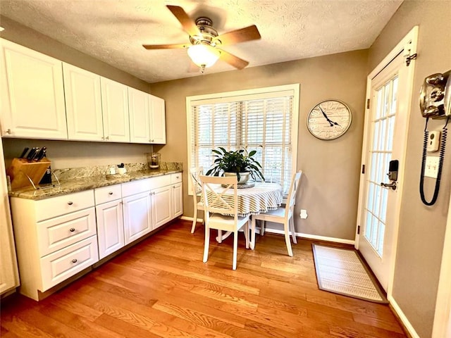 kitchen featuring white cabinetry, light wood-type flooring, light stone counters, and a textured ceiling