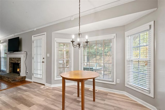 unfurnished dining area featuring a fireplace, an inviting chandelier, crown molding, and light hardwood / wood-style flooring