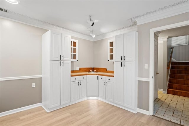 kitchen featuring butcher block counters, white cabinetry, light wood-type flooring, and ornamental molding