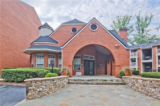 view of exterior entry with french doors, brick siding, a chimney, and roof with shingles