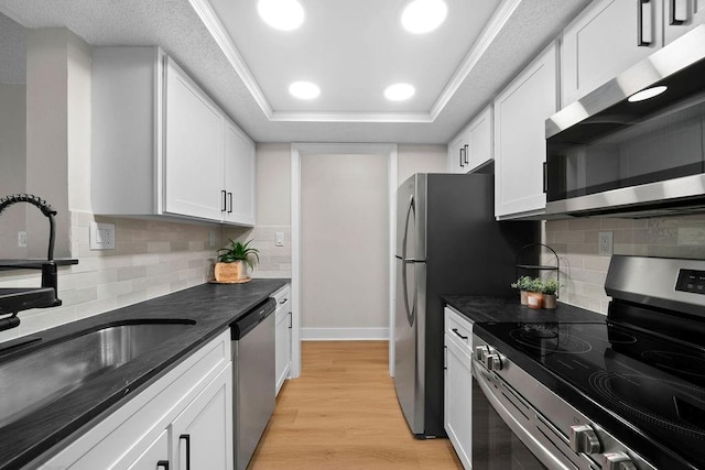 kitchen with light wood-style flooring, appliances with stainless steel finishes, a tray ceiling, white cabinetry, and a sink