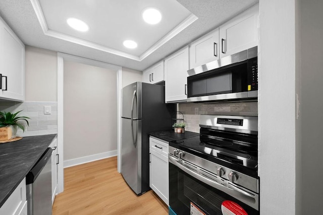 kitchen with light wood finished floors, dark countertops, a tray ceiling, stainless steel appliances, and white cabinetry