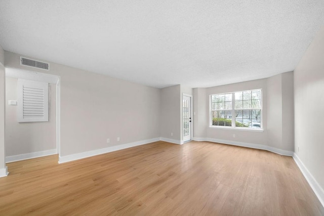 spare room featuring light wood finished floors, baseboards, visible vents, and a textured ceiling