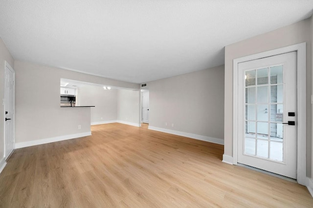 unfurnished living room with baseboards, visible vents, and light wood finished floors