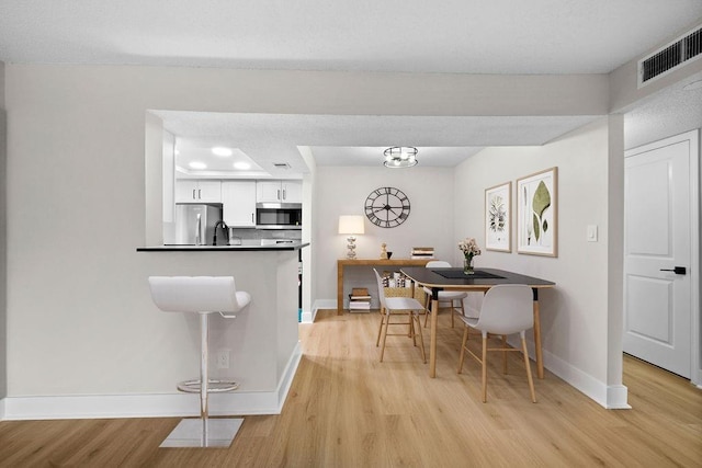 dining area with light wood-style floors, visible vents, and baseboards