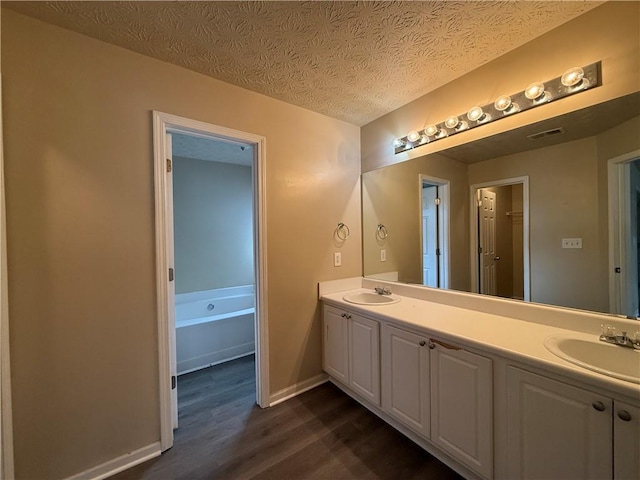 full bathroom with visible vents, double vanity, wood finished floors, a textured ceiling, and a sink