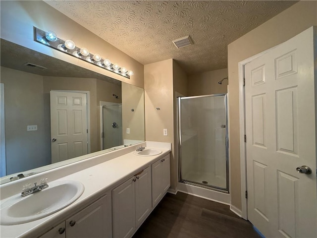 full bathroom with wood finished floors, visible vents, double vanity, a sink, and a shower stall