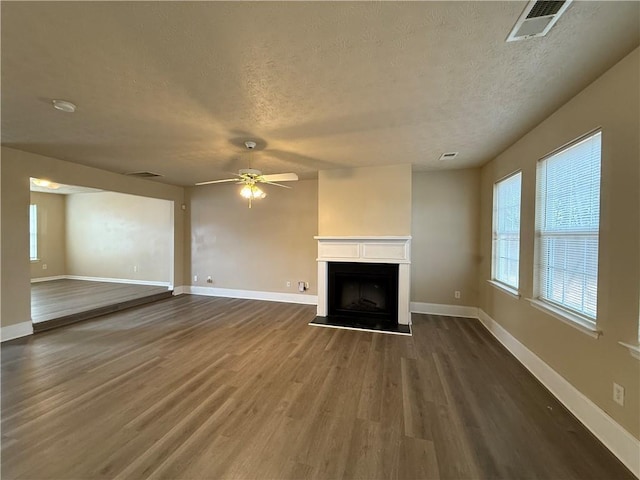 unfurnished living room with visible vents, a fireplace with raised hearth, baseboards, wood finished floors, and a textured ceiling