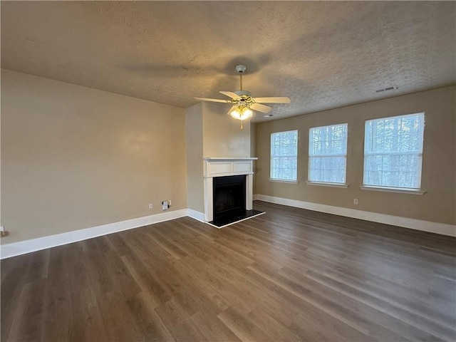 unfurnished living room with visible vents, a fireplace with raised hearth, a textured ceiling, baseboards, and dark wood-style flooring