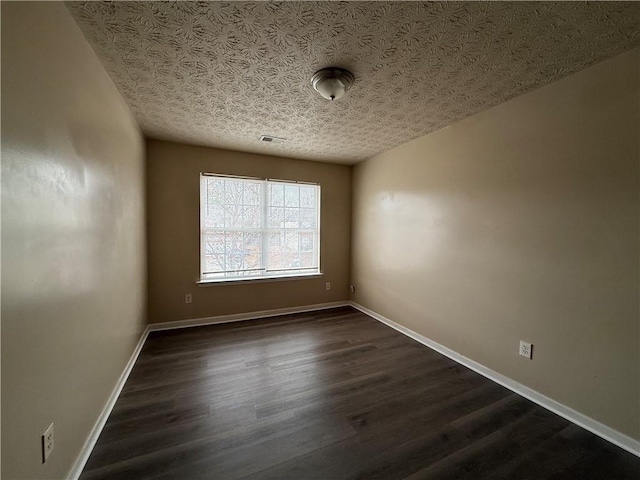 spare room featuring dark wood finished floors, visible vents, baseboards, and a textured ceiling