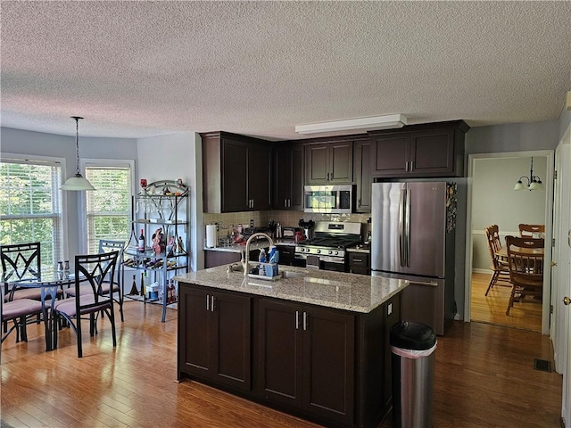 kitchen featuring tasteful backsplash, dark brown cabinets, stainless steel appliances, and hanging light fixtures