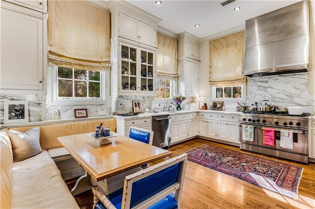 kitchen with wall chimney range hood, tasteful backsplash, wood finished floors, appliances with stainless steel finishes, and light countertops