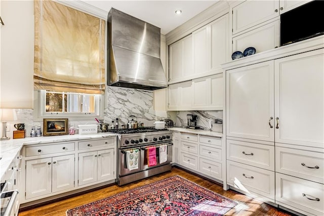 kitchen featuring backsplash, range with two ovens, wall chimney exhaust hood, and white cabinets