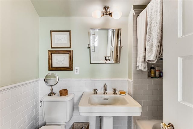 bathroom with a sink, toilet, tile walls, and wainscoting