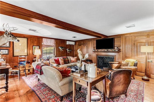 living room featuring wooden walls, an AC wall unit, beam ceiling, light wood-style flooring, and a fireplace