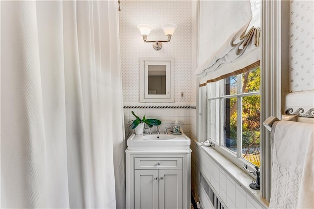 bathroom with radiator, wallpapered walls, vanity, wainscoting, and tile walls