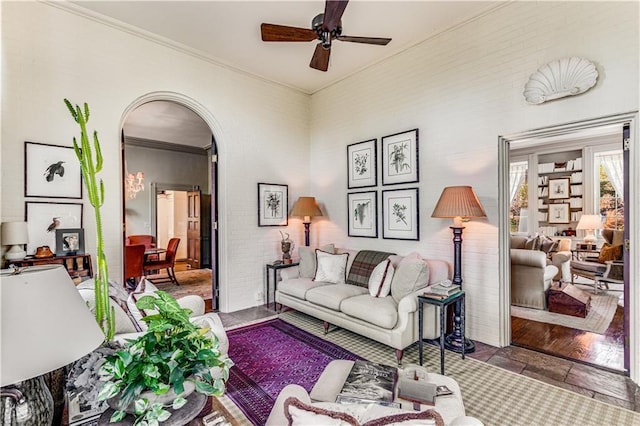 living area with arched walkways, ornamental molding, and a ceiling fan