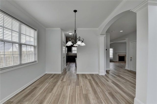 unfurnished dining area featuring ornamental molding, light wood-type flooring, a fireplace, and arched walkways