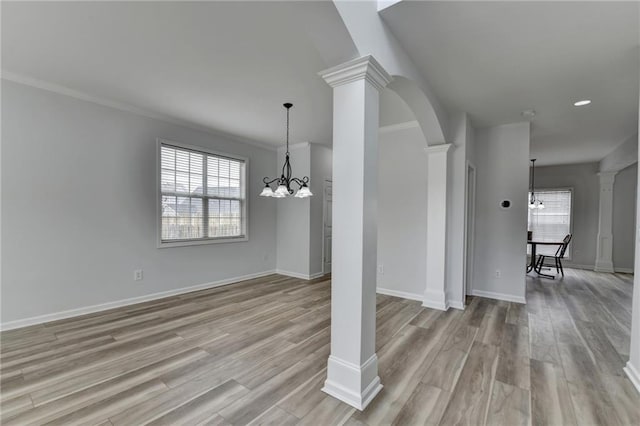 unfurnished dining area featuring decorative columns, light wood-style flooring, and a notable chandelier