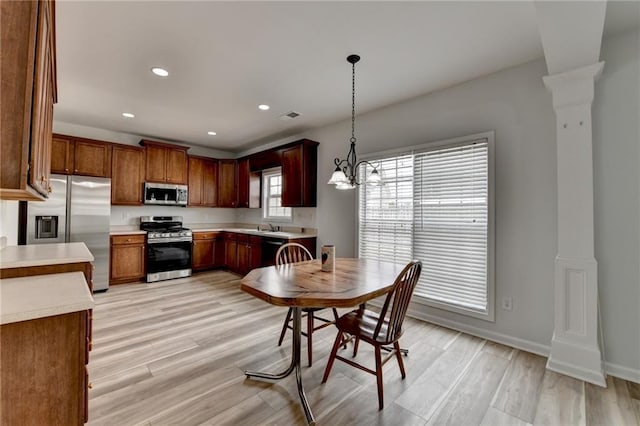 kitchen featuring stainless steel appliances, light wood-type flooring, light countertops, and decorative columns