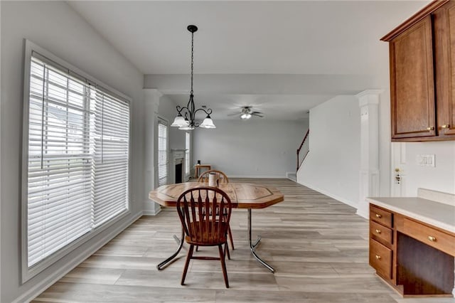 dining room with ceiling fan with notable chandelier, a fireplace, baseboards, stairway, and light wood-type flooring