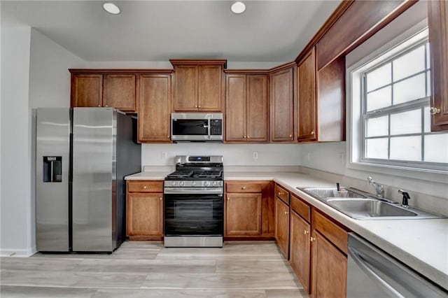 kitchen with light countertops, appliances with stainless steel finishes, a sink, and brown cabinets