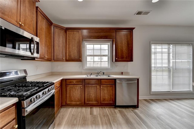 kitchen featuring light wood finished floors, light countertops, appliances with stainless steel finishes, and a sink