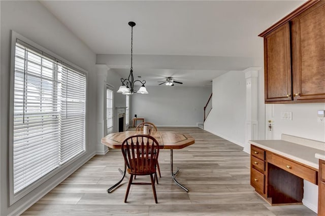 dining area with ceiling fan with notable chandelier, a fireplace, baseboards, stairway, and light wood-type flooring