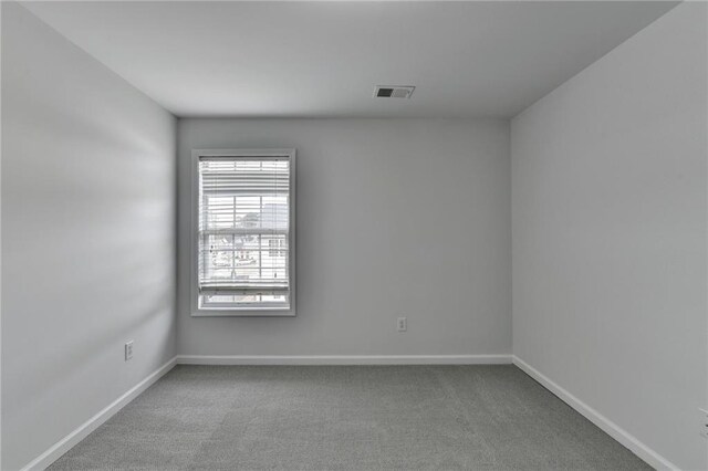 empty room with carpet, visible vents, and baseboards