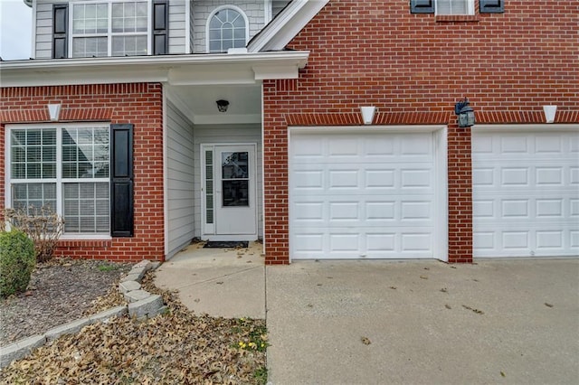 property entrance with a garage, brick siding, and driveway