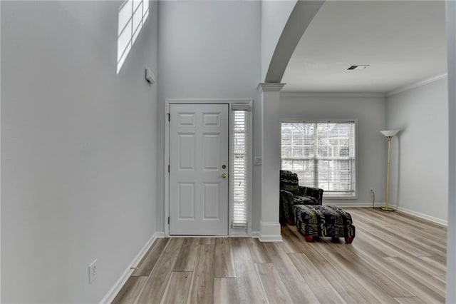 entrance foyer featuring light wood finished floors, decorative columns, visible vents, arched walkways, and baseboards