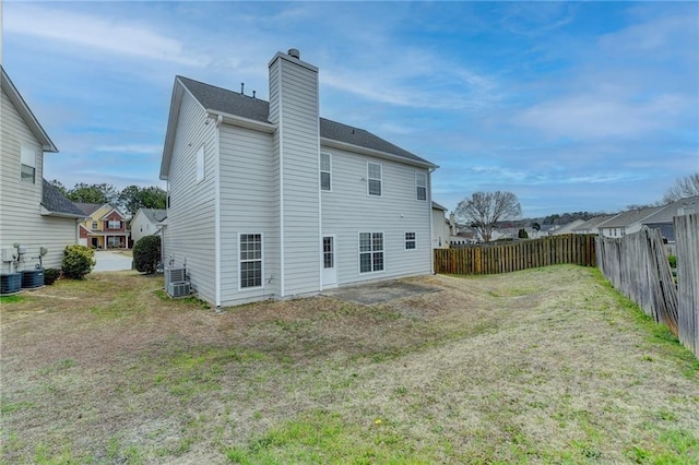 rear view of house with central AC unit, a chimney, fence, and a lawn