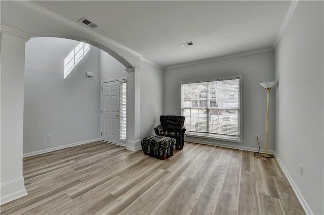 unfurnished room with arched walkways, crown molding, light wood-style flooring, and baseboards