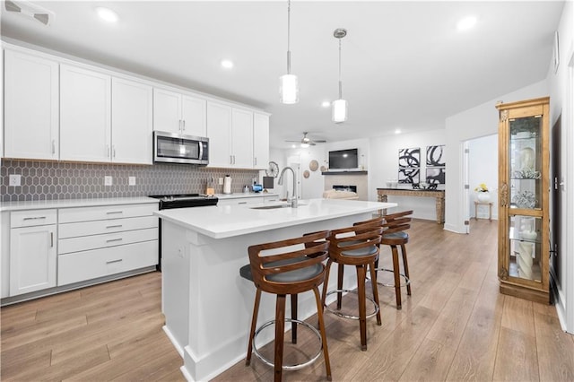 kitchen featuring sink, white cabinetry, stainless steel appliances, a center island with sink, and decorative light fixtures