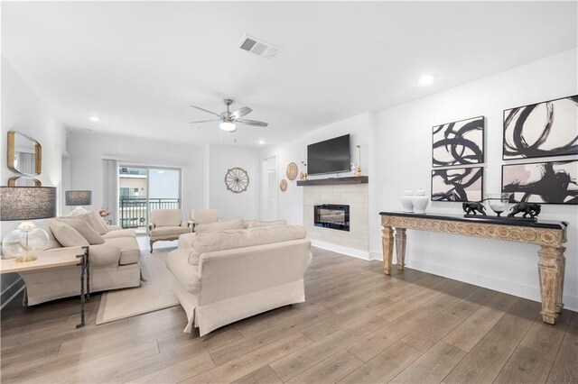 living room with a tile fireplace, hardwood / wood-style floors, and ceiling fan