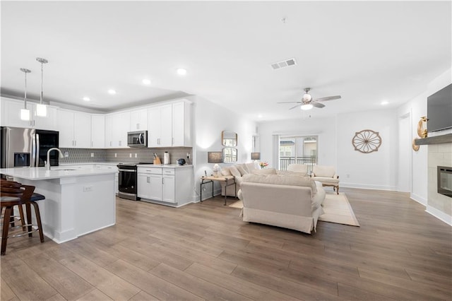 kitchen featuring white cabinetry, hanging light fixtures, a center island with sink, and appliances with stainless steel finishes