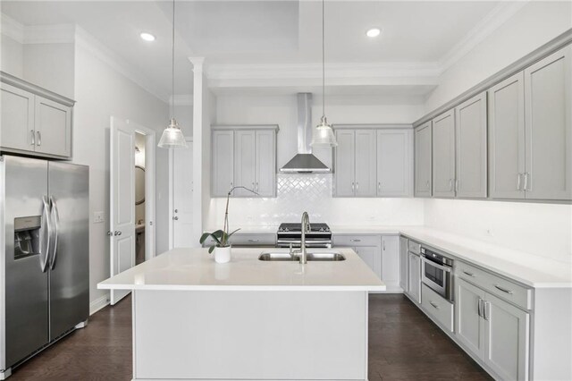 kitchen with a center island with sink, wall chimney exhaust hood, stainless steel appliances, pendant lighting, and sink