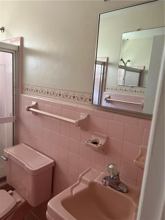 bathroom featuring toilet, tile walls, a sink, and wainscoting