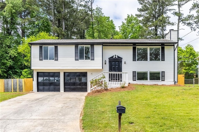 bi-level home featuring a chimney, fence, a garage, a front lawn, and concrete driveway
