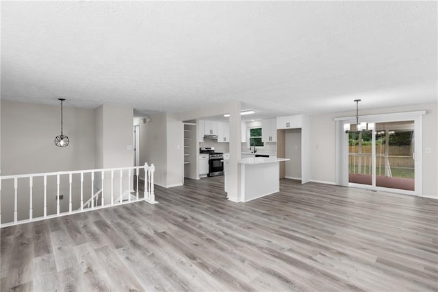unfurnished living room with a textured ceiling, a chandelier, light wood finished floors, and baseboards